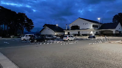 夜間の駐車場。照明が明めで、路面はフラットです。奥に図書館の建物が見えます。