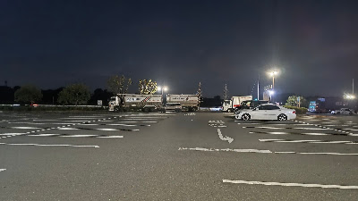 夜間の乗用車エリア。照明はあるものの、大型トラックが近めに停まっています。