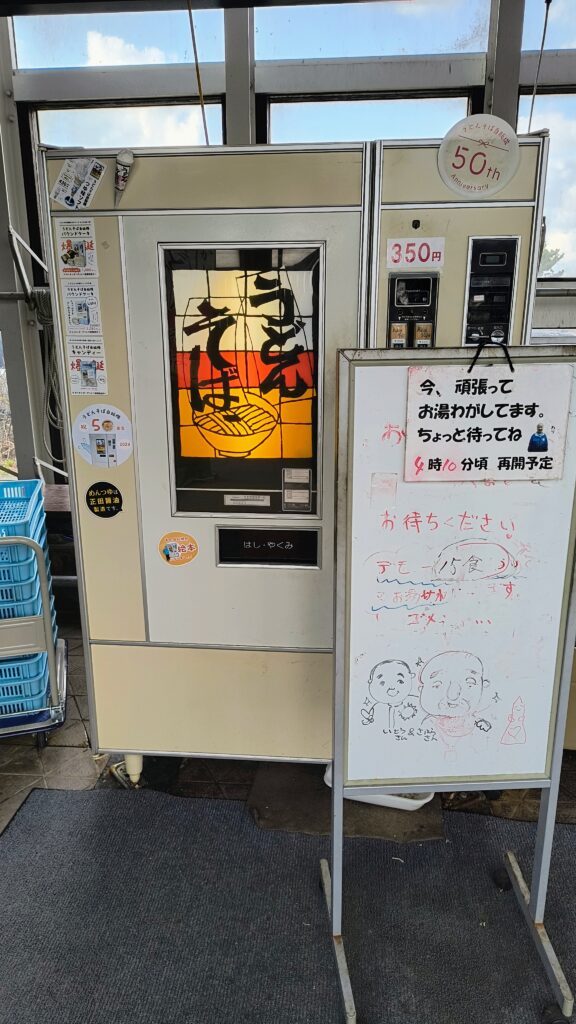 うどんそば自販機。ホワイトボードに湯沸かし中の文字。