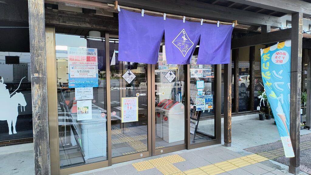 夜、閉店後の道の駅そうま物産館入口。紫の暖簾と営業時間9:30〜18:00の表示が見える。